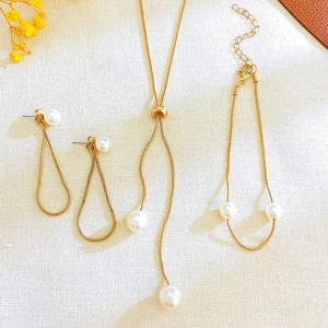 Detail of gold pearl jewelry set including long drop earrings and Y-shaped necklace
