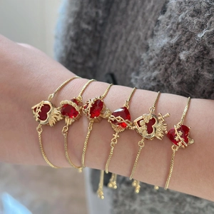 Primo piano di braccialetti d'oro regolabili con ciondoli a cuore rosso sul polso