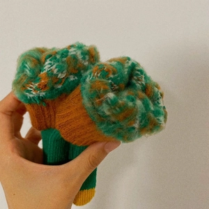 Detail shot of tricolor knitted leg warmers in green, brown, and yellow wool blend