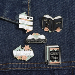 Detail of vintage enamel book pins set with creative text on dark denim fabric background