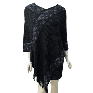 Detail shot of black knitted poncho with blue diamond pattern and elegant tassel fringe