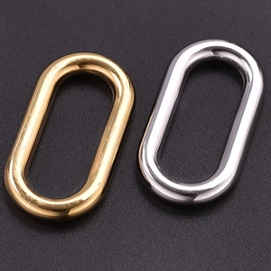 Polished gold and silver stainless steel oval pendant rings on a black textured surface