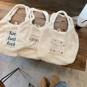 Drei Plüsch-Einkaufstaschen aus Lammwolle mit Luck- und Smile-Stickerei auf Holzbank