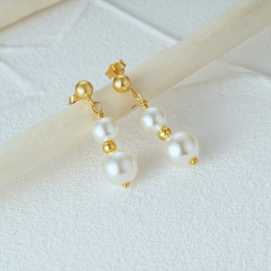 Detail of 925 silver pearl drop earrings with gold plating on white textured stand