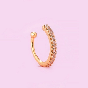 Macro shot of gold C-shaped ear cuff with pave white zircons on pink background