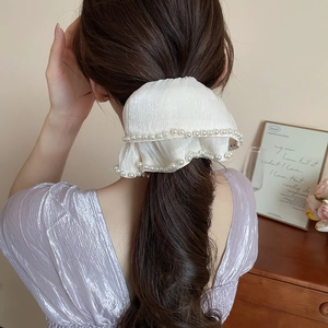 Detailed back view of a creamy white satin scrunchie with pearls on a messy ponytail