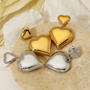 Polished hollow heart drop earrings in gold and silver finish on marble tray