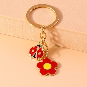 Detail shot of red enamel ladybug and flower charms on a golden metal keychain ring