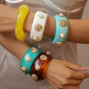 Detailed view of resin bangles with gold shell accents and faux pearls in various colors