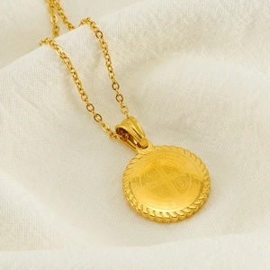 Golden Saint Benedict medal pendant necklace on white textured fabric background