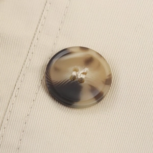 Close-up of tortoiseshell resin button and reinforced stitching on khaki trench coat