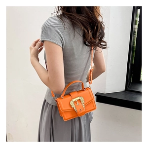 Detail of orange handbag showing the golden baroque buckle and sleek glossy texture