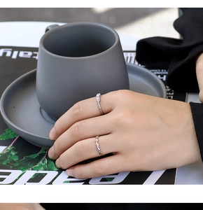 Silver geometric textured ring and zircon band shown on hand with ceramic cup