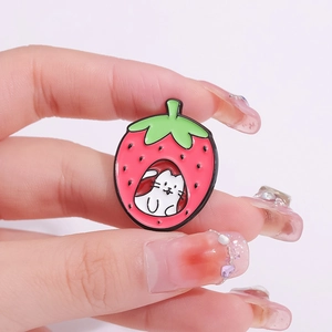 Cartoon enamel pin featuring a red strawberry and cute white cat held by manicured hand