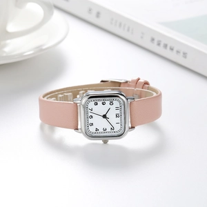 Vue détaillée d'une montre carrée argentée avec bracelet en cuir rose près d'un café