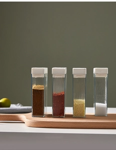 Detailed view of four clear spice jars with white lids on a wooden board for kitchen storage