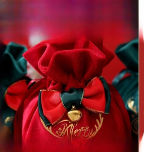 Close-up of red velvet Christmas gift bag with gold stamping, bow, and small bell