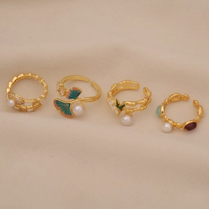 Detailed macro shot of four gold open rings with pearls, enamel leaves, and gemstones