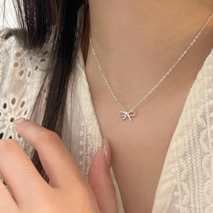 Close-up of elegant silver bow pendant necklace on model wearing white lace dress