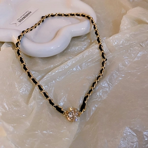 Détail d'une chaîne tressée en or et cuir noir avec pendentif boule en strass brillant