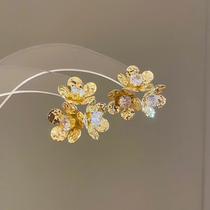 Macro shot of gold flower earrings with zircon center and hammered metal texture