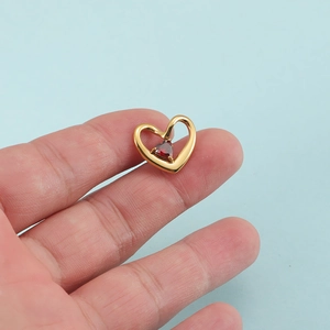 Pendentif cœur doré avec pierre de naissance rouge tenu entre les doigts sur fond bleu