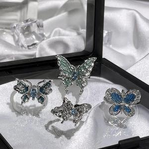 Detail shot of four butterfly rings with blue enamel and sparkling gems on white silk