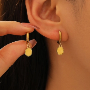 Détail de créole dorée avec un pendentif disque en métal texturé soleil sur l'oreille