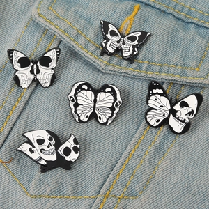 Gothic black and white skull butterfly enamel pins pinned on a blue denim jacket