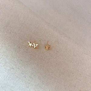 Asymmetric gold flower earrings with dainty floral studs on natural linen background