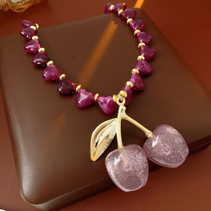 Detail of purple acrylic cherry pendant on gold chain over premium brown leather box
