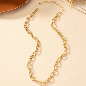 Hip-hop style gold chain necklace with textured twist links on a beige surface