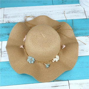 Détail d'un chapeau de paille kaki avec bord ondulé et décorations florales colorées