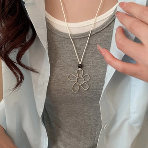 Close-up of a silver flower pendant on a white cord worn over a light blue shirt