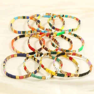 Detail view of colorful Tila bead bracelets with gold accents on silk fabric