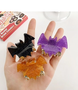 Close-up of glittery bat-shaped acrylic hair claws in black, purple, and orange colors