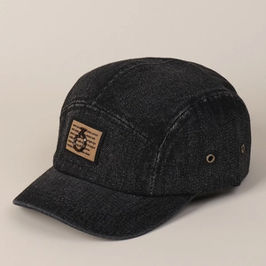 Detail van zwarte denim baseballpet met bruine patch en opvallende metalen ringaccent
