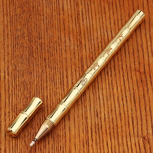 Macro detail of golden bamboo-shaped brass pen with Chinese calligraphy on wood