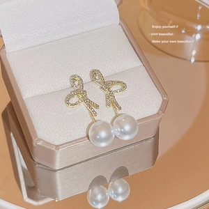 Detail of gold bow earrings with zircon stones and elegant hanging white pearls