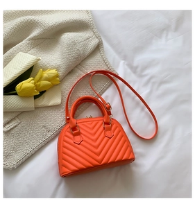 Close-up of orange V-quilted shell bag with matching handle and adjustable leather strap