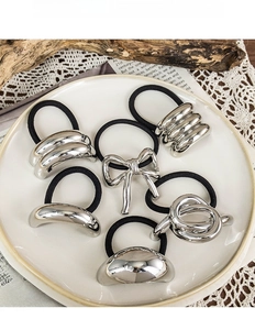 Set of six silver metallic hair ties with bows and knots on white ceramic tray