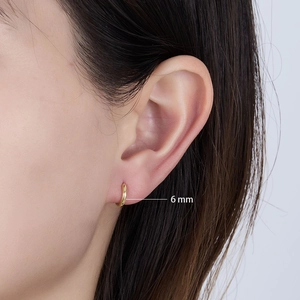 Close-up of a small 6mm golden sterling silver hoop earring worn on a model ear