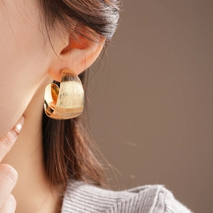 Close-up of golden C-shaped hoop earrings with brushed metal texture on female model