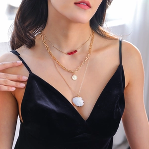 Detail view of multi-layer gold necklace featuring coral beads, coin and natural shell pendant