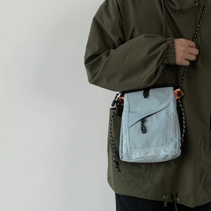 On-model view of a light blue canvas crossbody bag with orange accents and drawstrings