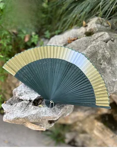Detail of dark green Chinese fan with gold trim and hollow carved bamboo ribs on stone