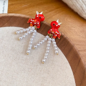 Detail of red enamel horse earrings with pearl tassels on a textured wooden tray