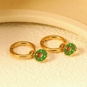 Golden Christmas wreath earrings with green ring and red bow on a white stone base