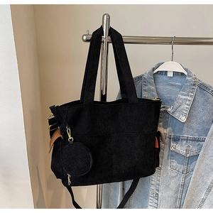 Detail of black corduroy tote bag featuring orange label and matching round coin purse