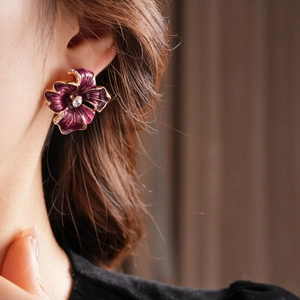 Detail of purple enamel flower earring with gold trim and crystal center on model